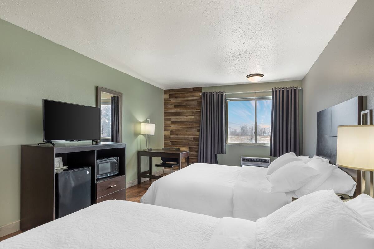 A hotel room with two beds, a desk, a television, and a window with curtains.