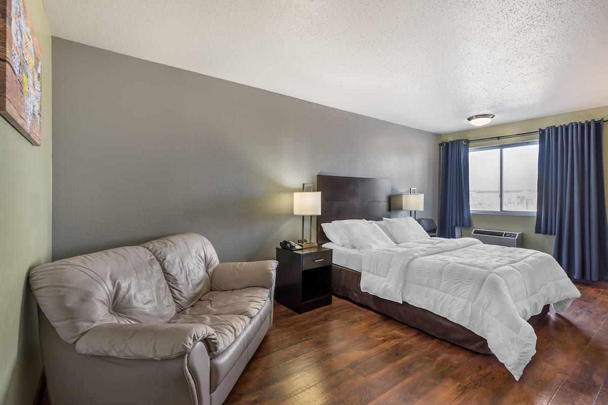 A hotel room with a sofa, a bed, a nightstand with a lamp, and a window with curtains.