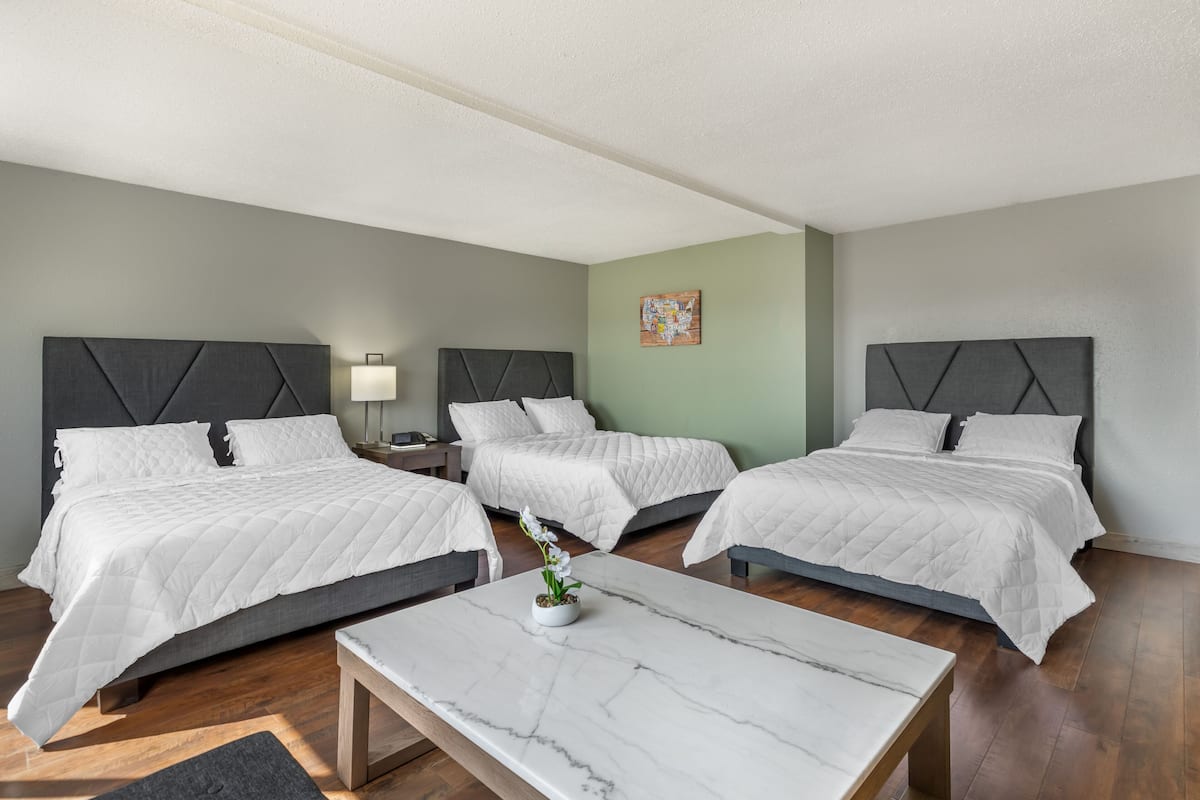 A hotel room with three beds, a marble coffee table, and a nightstand with a lamp.
