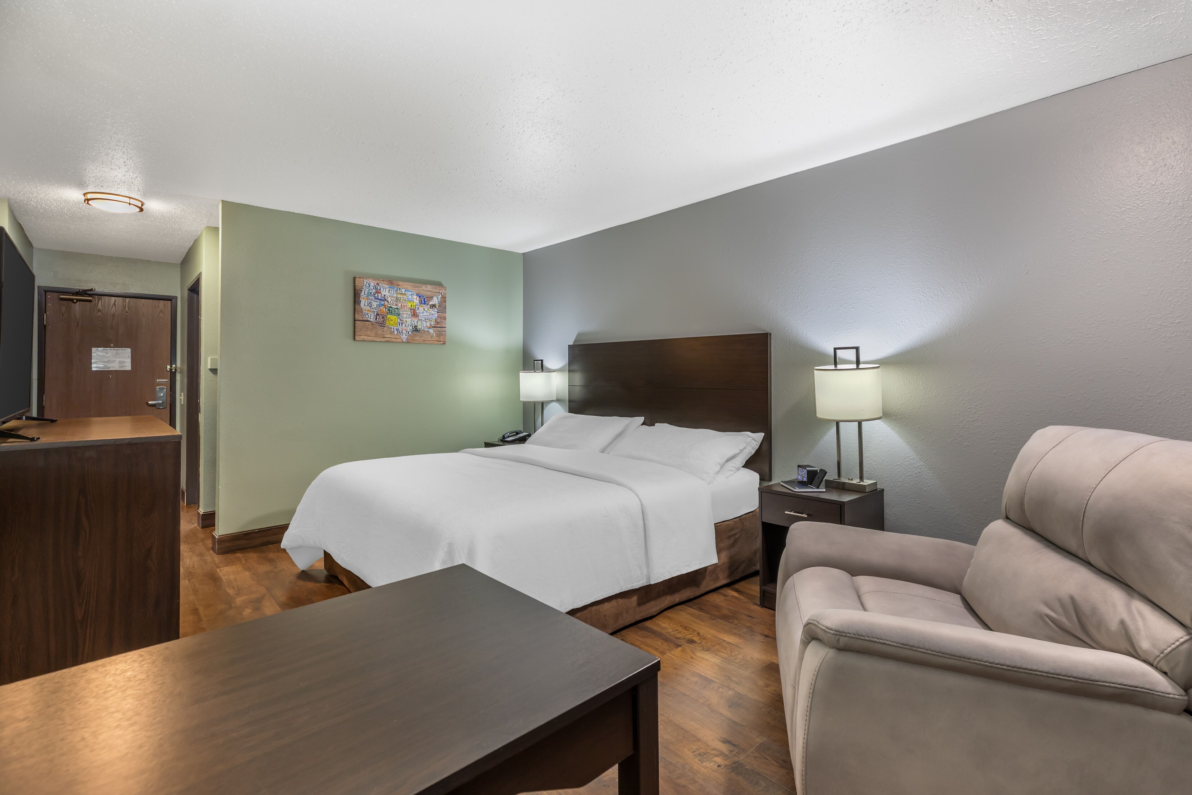 A hotel room with a bed, a desk, a chair, a nightstand, and a lamp.
