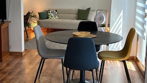 A dining area with a round table, four chairs, and a sofa in the background.