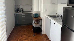 A compact kitchen with white cabinets, a microwave, a sink, and a herringbone-patterned floor.