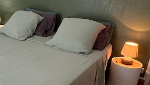 A bed with a green bedspread and pillows, a bedside lamp, and a round nightstand.