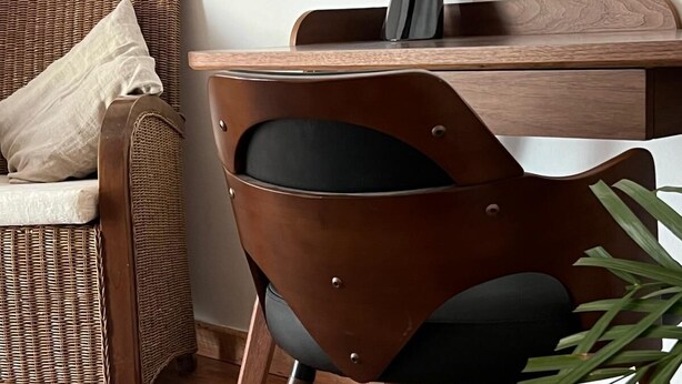 A modern dining area with a wooden dining table, a wicker chair, and a contemporary chair with a black cushion.