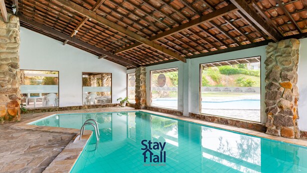 An indoor swimming pool with stone walls and a wooden ceiling, large windows, and a sign reading "Stay Fall short term rental". - Casa de Campo Familiar em Gravata 065D (Gravata)