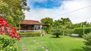 A house with a tiled roof, surrounded by a well-maintained garden with a lawn, stepping stones, and various plants. - Casa de Campo Familiar em Gravata 065D (Gravata)