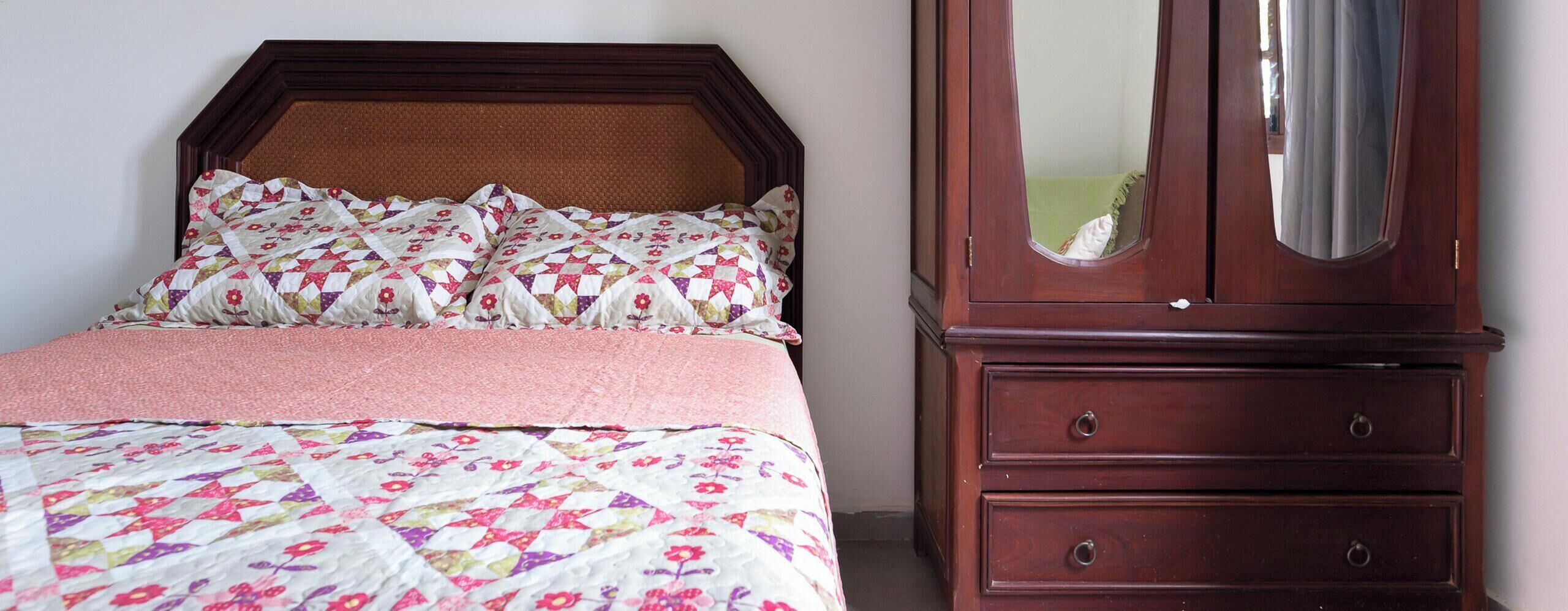 Un lit avec une couette à motifs floraux et une tête de lit en bois, une commode avec des tiroirs et un miroir.