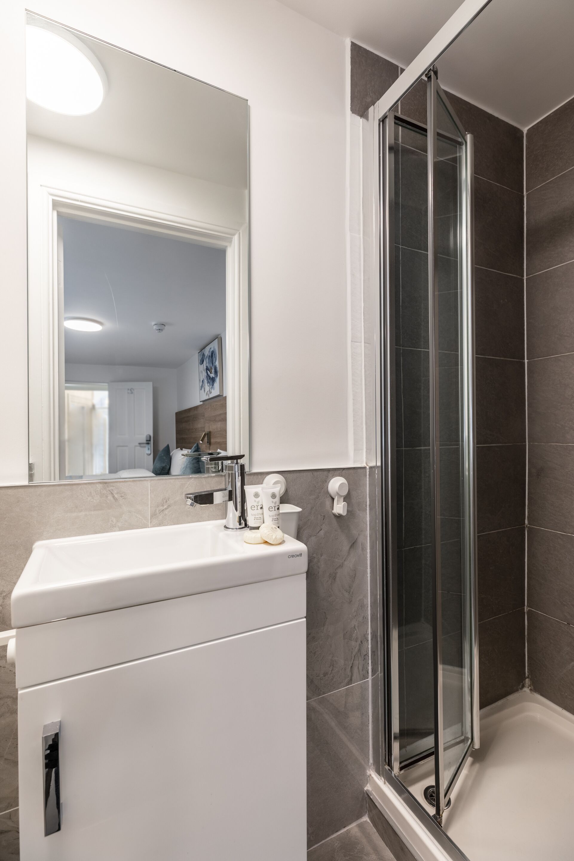 A modern bathroom with a white sink, a glass shower enclosure, and a large mirror.