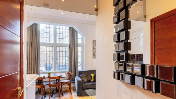 A modern living room with a dining area, large windows, and a unique wall-mounted display. - Griffin House Hotel  (London)
