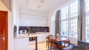 A modern kitchen with white cabinets, a marble backsplash, and a dining area with wooden chairs and a table. - Griffin House Hotel  (London)
