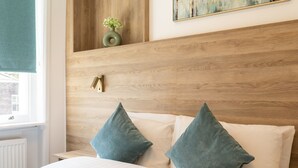 A bedroom with a wooden headboard, two pillows, a bedside table, and a window with a view of a building. - Griffin House Hotel  (London)