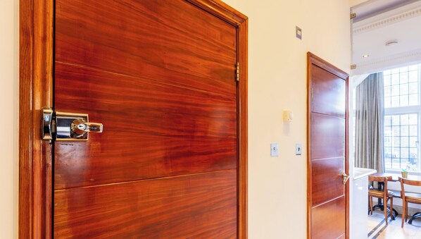 A wooden door with a lock, a wall socket, and a window with curtains. - Griffin House Hotel  (London)