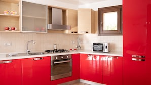 A modern kitchen with red cabinets, stainless steel appliances, and a window above the sink. - Casa Della Vigna 3 by Wonderful Italy (Laerru)