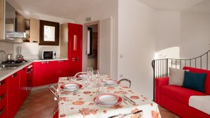 A compact kitchen with red cabinets, a dining table set for four, and a red sofa in the living area. - Casa Della Vigna 3 by Wonderful Italy (Laerru)