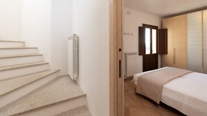 A bedroom with a bed, a wooden door, a radiator, and a staircase. - Casa Della Vigna 3 by Wonderful Italy (Laerru)