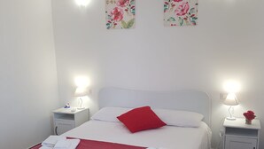 A neatly made bed with a red pillow and white linens, two bedside lamps, and floral artwork on the walls. - DE MEO GUEST HOUSE APPARTAMENT (Castellammare del Golfo)