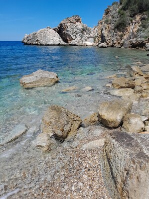 Una costa rocosa con aguas cristalinas y un edificio sobre las rocas.