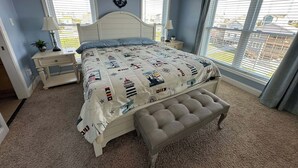 A bedroom with a bed, nightstands, a bench, and two windows with blinds. - 5-bedroom house with private pool, spa and elevator near Rodanthe Pier (Rodanthe)