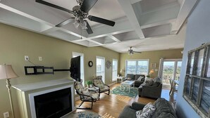 A spacious living room with a fireplace, ceiling fans, and large windows offering views of the city. - 5-bedroom house with private pool, spa and elevator near Rodanthe Pier (Rodanthe)