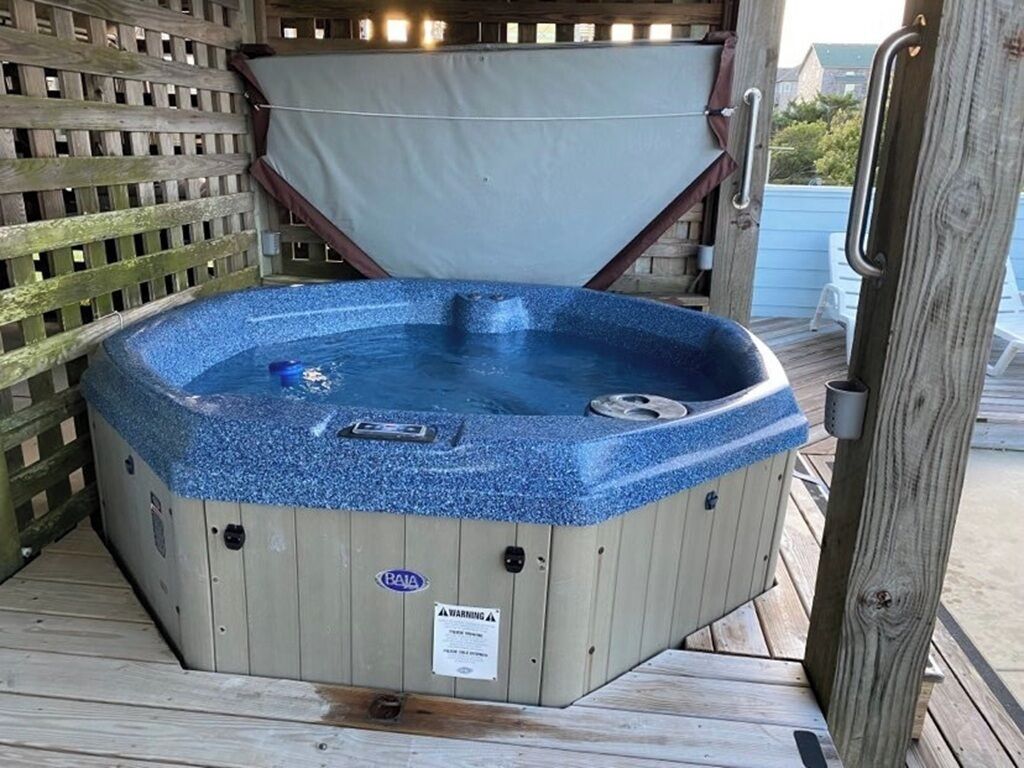 A hot tub with a wooden deck and a wooden fence in the background.