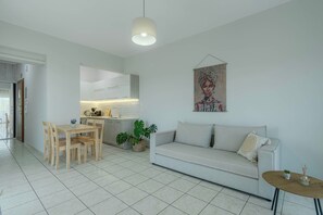Una sala de estar moderna con sofá, una mesa de comedor con sillas, una zona de cocina y una obra de arte colgada.