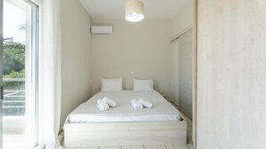 A minimalist bedroom with a large bed, a ceiling light, and a view of greenery outside. - Joyful Guest House 2 Gaia by 8essentially (Galatas)