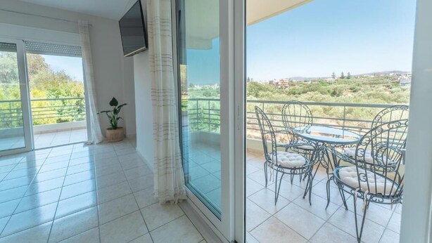 A balcony with a table and chairs, a potted plant, and a TV mounted on the wall. - Joyful Guest House 2 Gaia by 8essentially (Galatas)