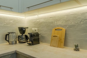 Una cocina con cafetera, molinillo y tabla de cortar de madera.