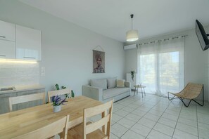 Una cucina moderna con mobili bianchi, un tavolo da pranzo con sedie, un divano, un piccolo tavolino e una sedia in vimini.