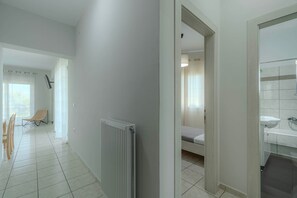 Een gang met een radiator, een bed en een badkamer met een wastafel.