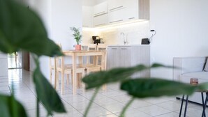 A modern kitchen with white cabinets, a wooden dining table, and a plant. - Joyful Guest House 2 Gaia by 8essentially (Galatas)