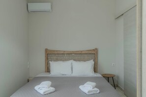 A single bed with a wooden headboard, two white pillows, and two folded towels on a textured grey bedspread.
