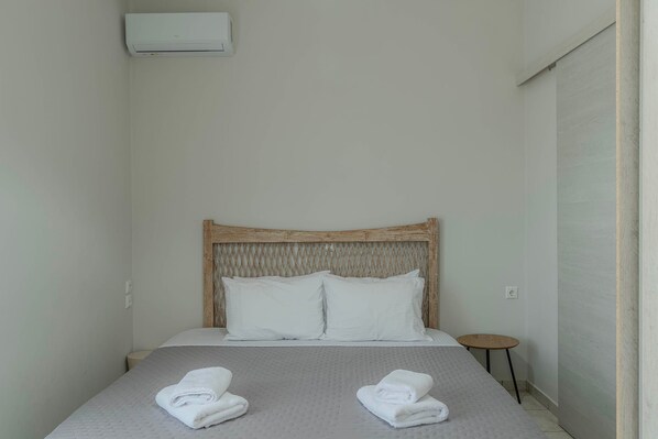 A single bed with a wooden headboard, two white pillows, and two folded towels on a textured grey bedspread.