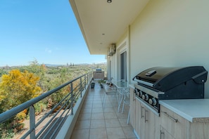 Een balkon met een barbecue, een tafel met stoelen en uitzicht op het omliggende landschap.