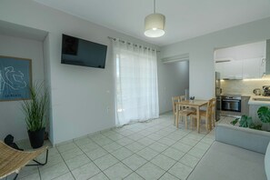 Un soggiorno moderno con televisione a schermo piatto, un tavolo da pranzo con sedie, un divano e un angolo cottura con piano cottura e lavello.