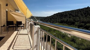 A balcony with a metal railing overlooking a road and a forested hill. - KRK Enjoy waterfalls, sun, beach and sea: Domicile Sunce Gudiča (Skradin)