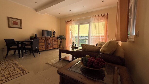 A living room with a sofa, a coffee table with fruit, a TV on a wooden cabinet, and a dining area with chairs and a table. - KRK Enjoy waterfalls, sun, beach and sea: Domicile Sunce Gudiča (Skradin)