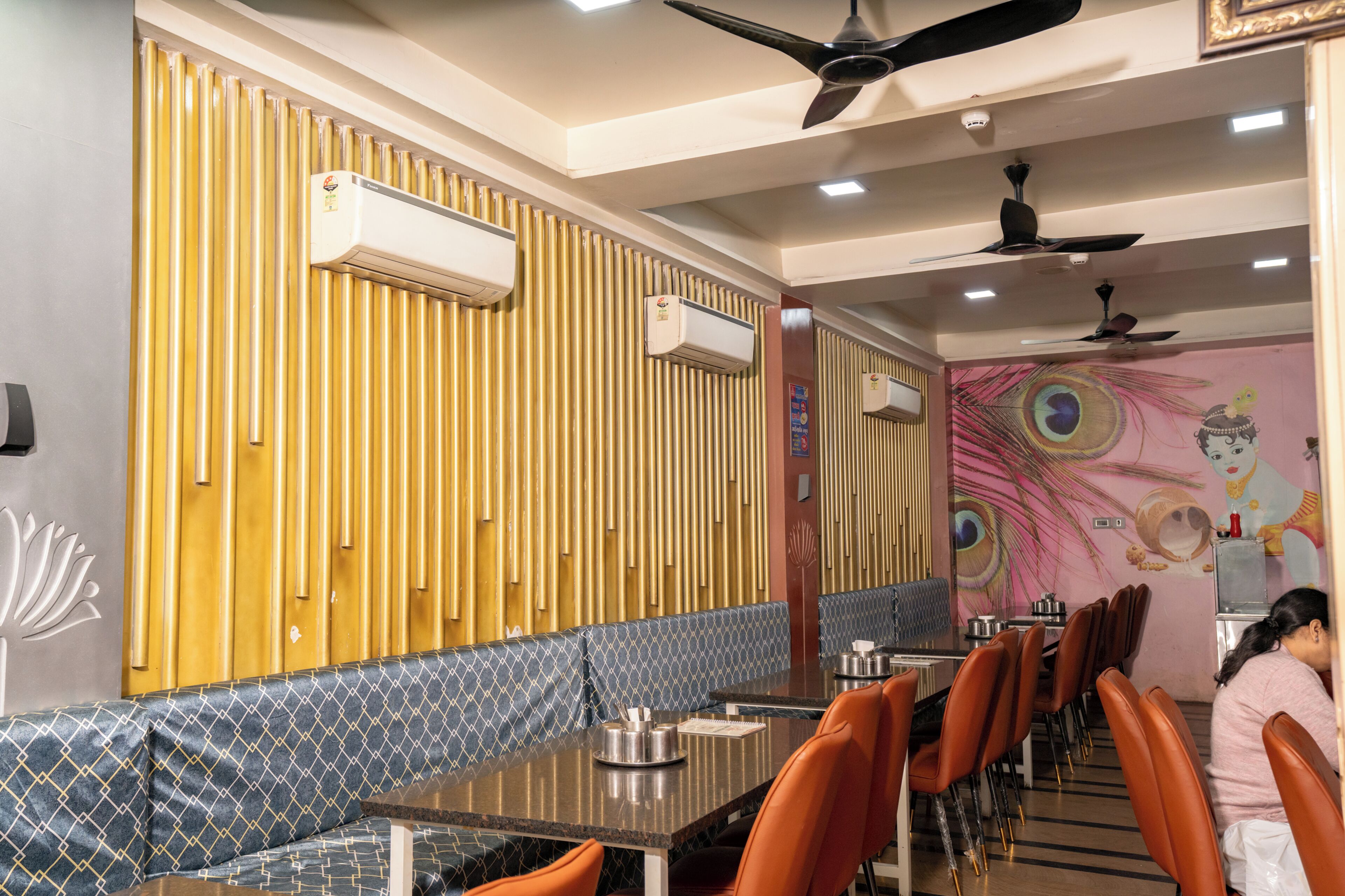 A restaurant with a long counter, orange chairs, and a decorative wall with vertical panels.