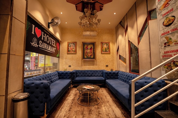A hotel lobby with a blue sectional sofa, a chandelier, framed artwork, and a sign reading "I ♥ HOTEL SAWAMANI".