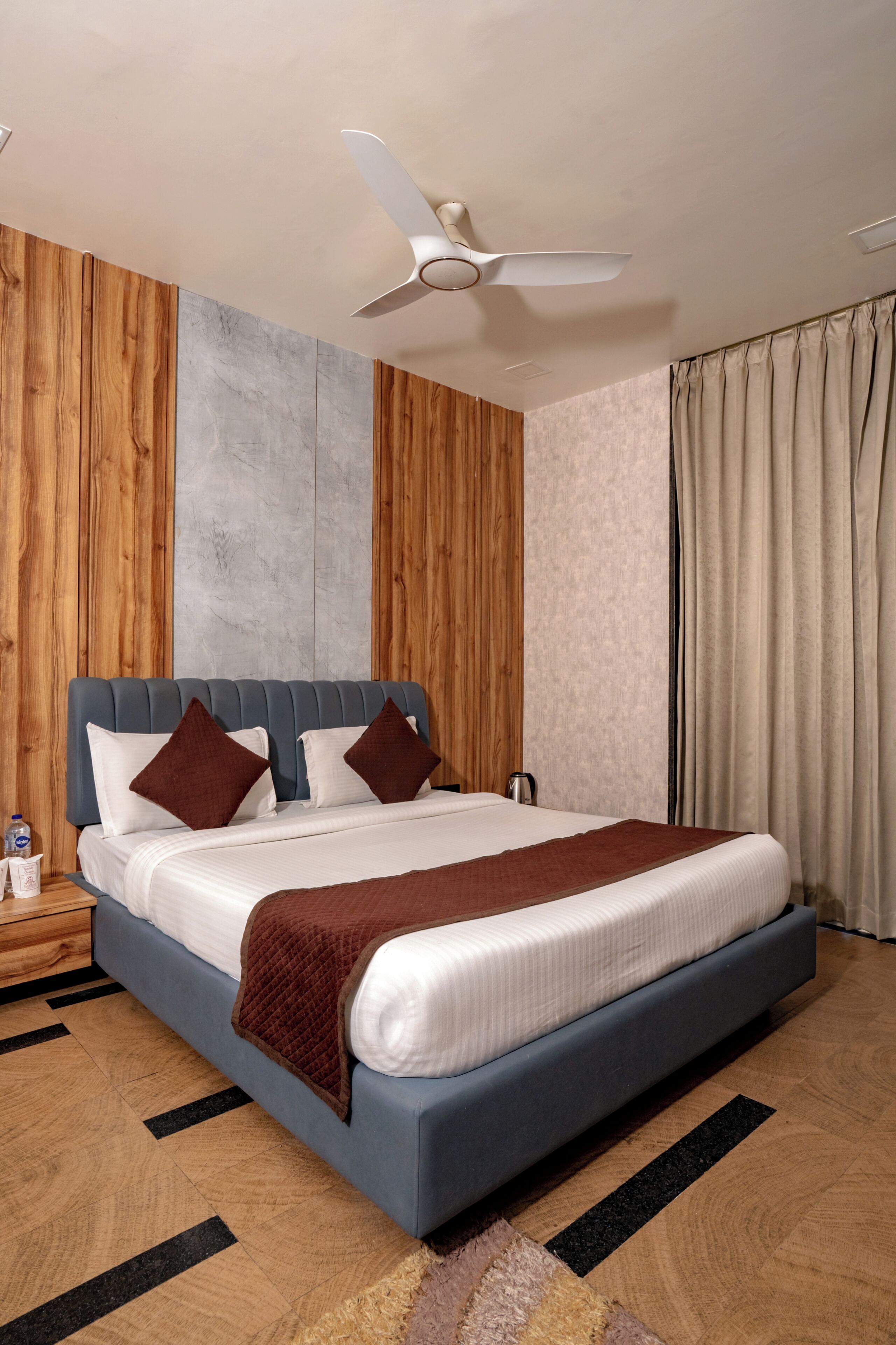 Ein modernes Hotelzimmer mit einem großen Bett, einem Deckenventilator, Holzwandverkleidung und Blick auf die Stadt.