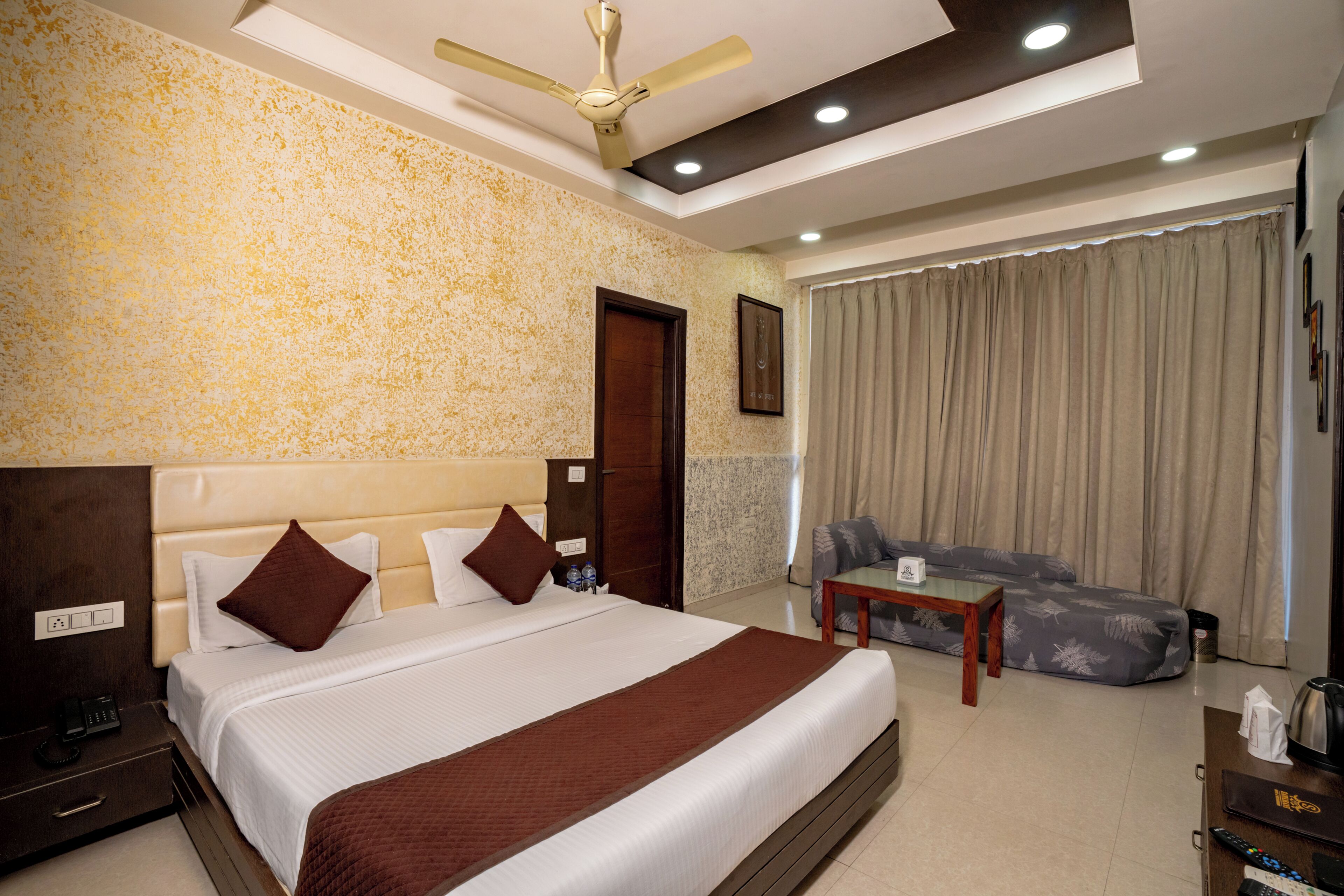 Quarto de hotel com uma cama grande, um ventilador de teto, um sofá e uma pequena mesa.