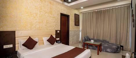 Quarto de hotel com uma cama grande, um ventilador de teto, um sofá e uma pequena mesa.