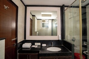 A bathroom with a wooden vanity, a sink, a mirror, and a glass shower enclosure. - Hotel Sawamani and Restaurant (Danta Ramgarh)