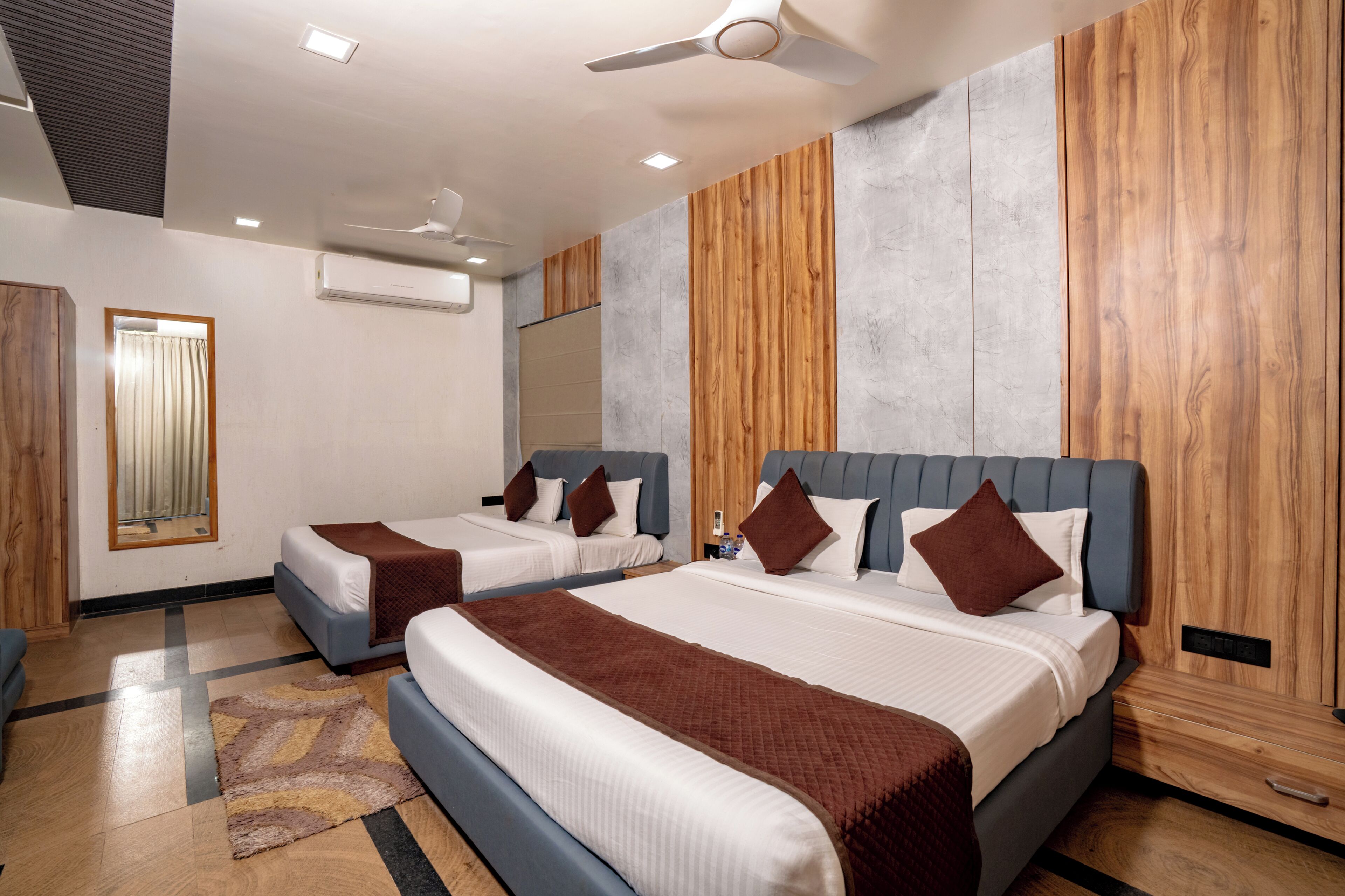 A hotel room with two beds, a ceiling fan, an air conditioning unit, and a mirror on the wall.