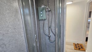 Un bagno moderno con doccia in vetro, porta carta igienica e tappetino.