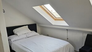 Una camera da letto con una finestra a lucernario, un letto, una sedia e un pavimento in legno.