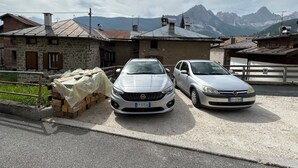 Dos coches aparcados frente a un edificio de piedra con techo metálico, al pie de montañas.