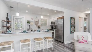 Una cocina moderna con armarios blancos, electrodomésticos de acero inoxidable y una isla central con taburetes de bar.
