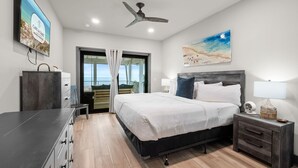 A modern bedroom with a bed, bedside tables, a ceiling fan, and a view of the sea through a glass door. - Magnolia by the Sea: Beachfront Home, Private Pool, Mother-In-Law, Secluded Beac (Indian Pass)