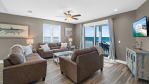 A spacious living room with a ceiling fan, a large window with a view of the ocean, and a television on the wall. - Beachfront Duplex Unit, Pet Friendly, Mexico Beach, Gorgeous Views! (Mexico Beach)